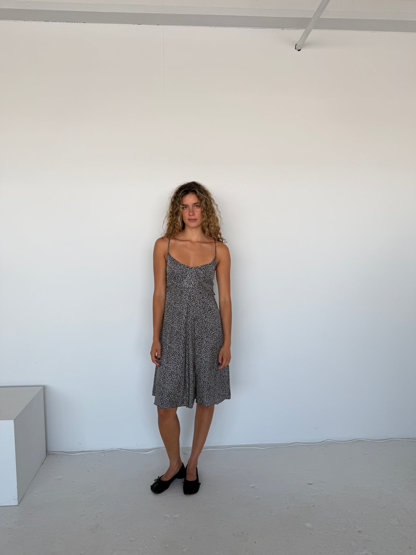 Woman in a patterned dress standing against a white wall.