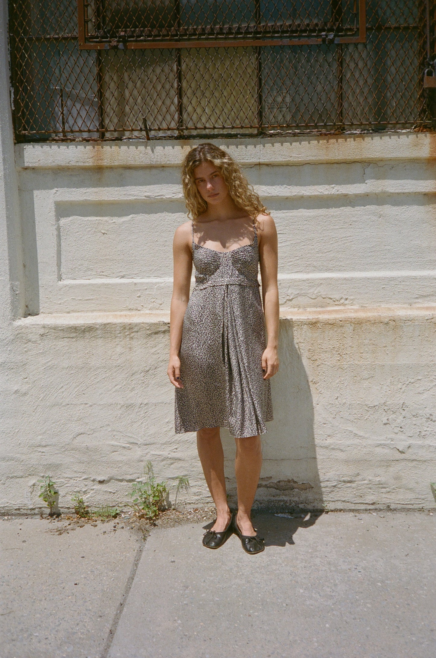 Woman in a patterned Balenciaga dress standing in front of an industrial building.